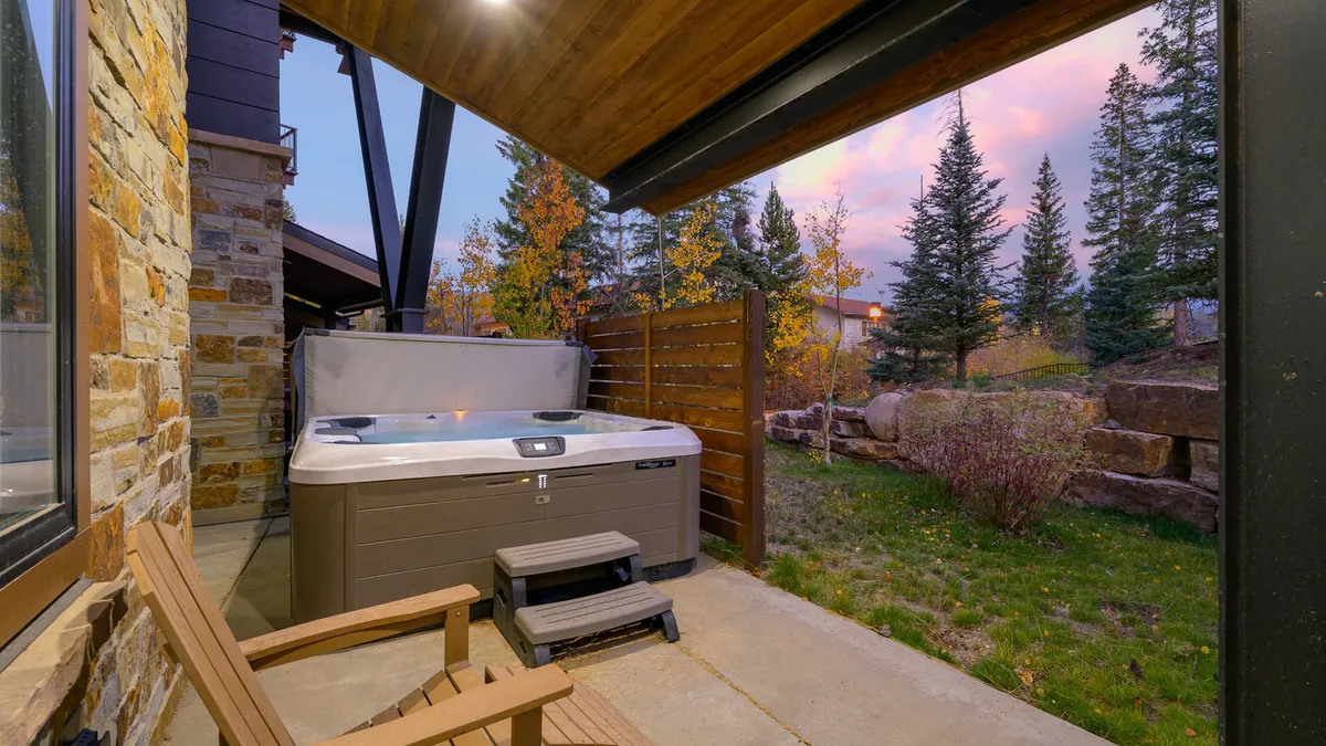 This image captures a private hot tub surrounded by wooden chairs and lush trees, creating a secluded oasis feel. The setting is perfect for soaking, enjoying nature, and stargazing, with the hot tub as the focal point and hints of the surrounding mountain landscape.