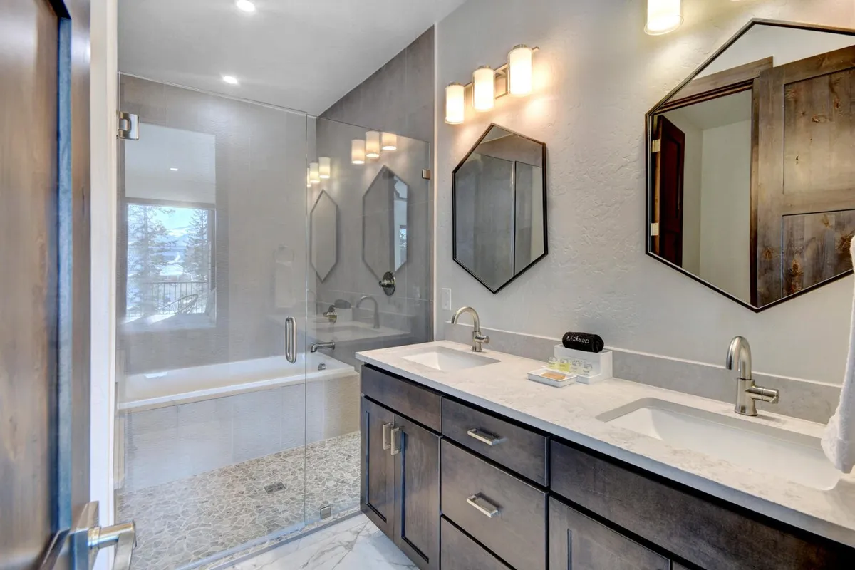 A luxurious bathroom featuring a double sink vanity, elegant glass shower enclosure, a freestanding bathtub, and modern lighting fixtures. The space is airy and calming, perfect for spa-inspired relaxation and rejuvenation.