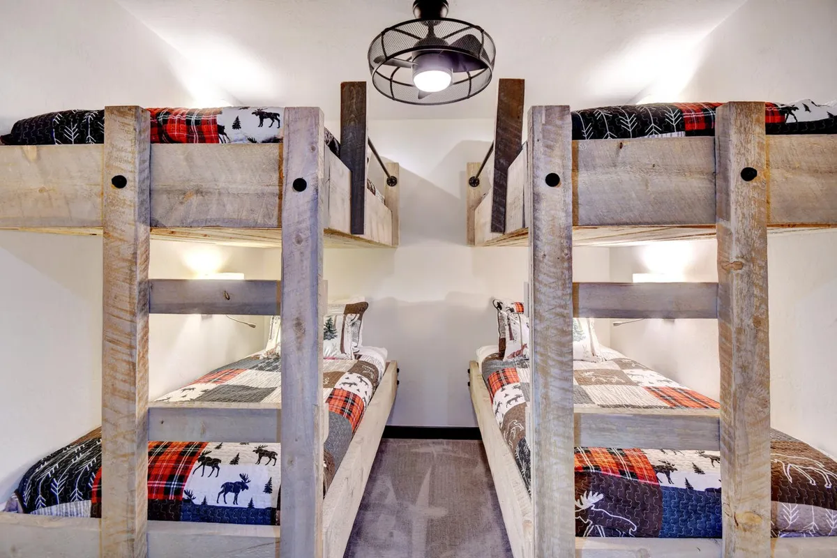 A playful bunkroom with four twin bunk beds dressed in plaid bedding, complemented by a whimsical light fixture. The design is both inviting and practical, fostering an atmosphere of fun and togetherness—perfect for children sharing stories at night.