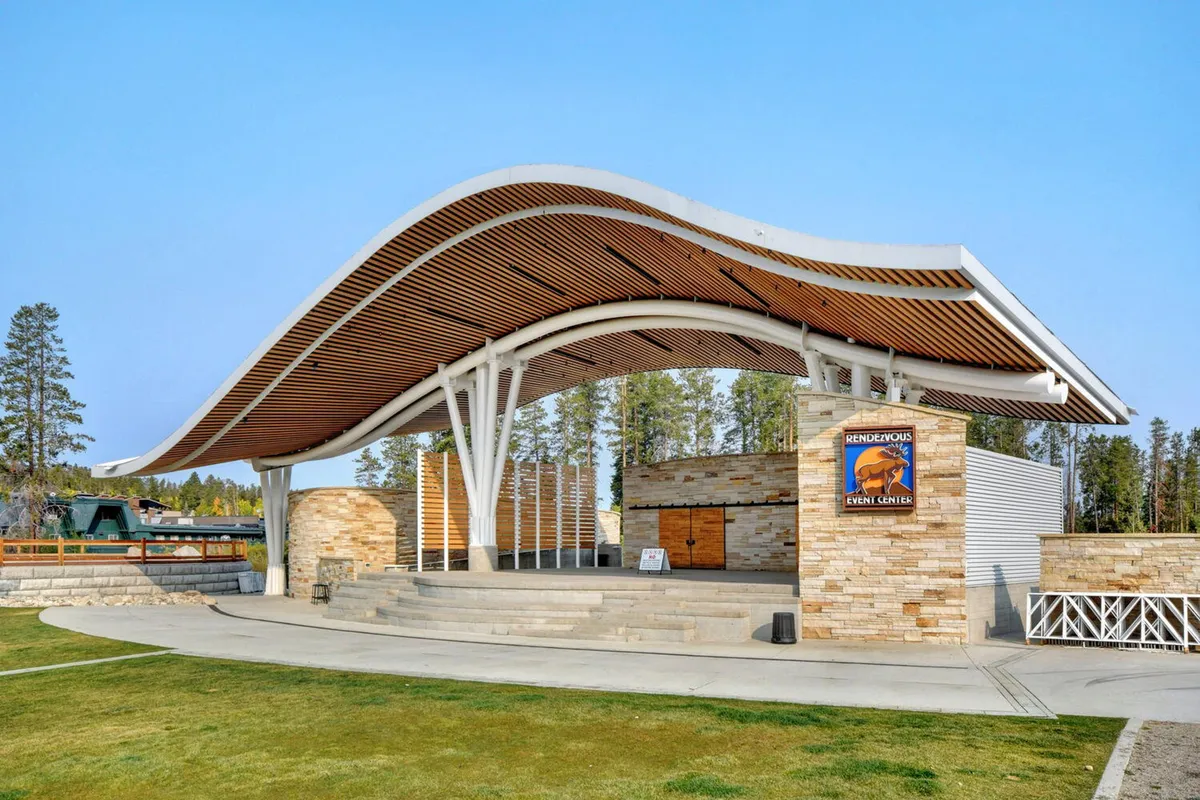 This image showcases the distinctive, curved-roof structure of the Hideaway Park amphitheater, with stone walls and an open stage area ready for outdoor community events and live performances. The setting is clearly designed for gatherings and entertainment.