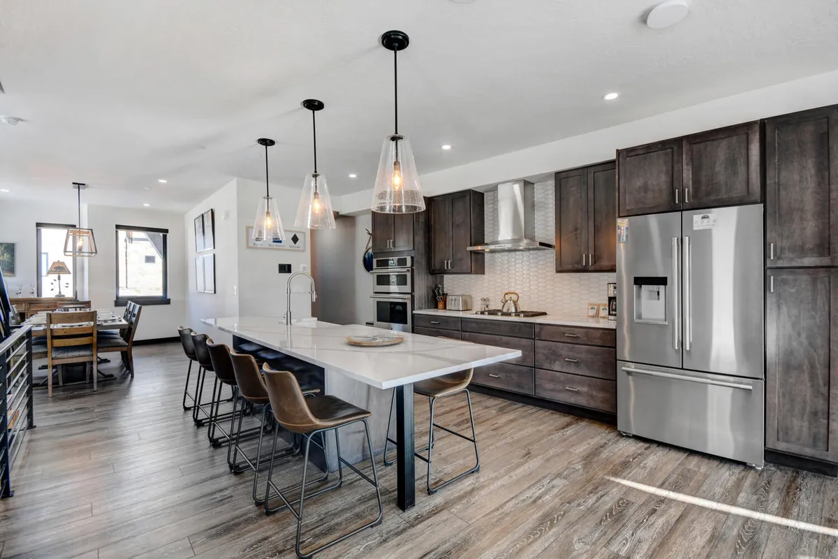 An open kitchen area with a prominent island, surrounded by bar stools and complemented by modern appliances and attractive lighting fixtures. The layout encourages interaction between those preparing food and those seated at the island, emphasizing communal dining and togetherness.