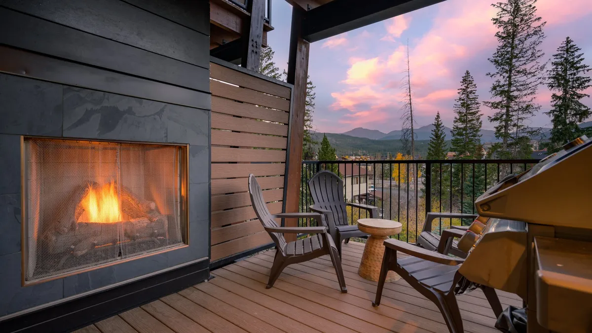 An inviting stone outdoor fireplace is framed by adirondack chairs, with a sweeping view of the mountains as the backdrop. The scene suggests warmth, connection, and relaxation—ideal for gatherings or quiet contemplation as the sun sets.