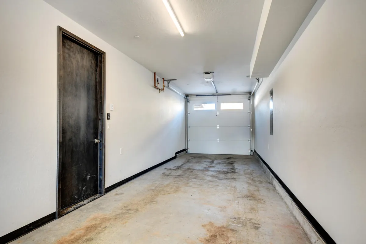 A clean, spacious garage with a sturdy garage door, black side door, and polished concrete floor. The setting is ideal for secure gear storage, bike maintenance, or prepping for outdoor adventures.
