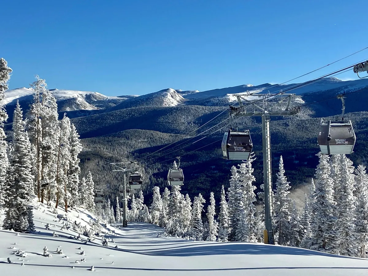 A panoramic exterior shot featuring ski lift gondolas gliding above snow-covered trees and a magnificent mountain range in the background. The scene captures the excitement of winter sports and the breathtaking alpine environment accessible from the property.