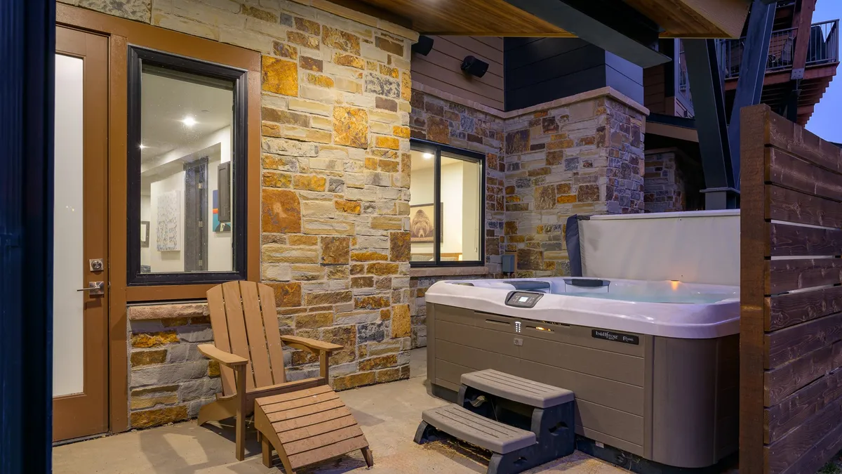 An exterior scene showing a private hot tub and Adirondack chairs set against a stone wall. The setup suggests relaxation and comfort, perfect for unwinding after a day of adventure, and hints at the amenities available to guests.