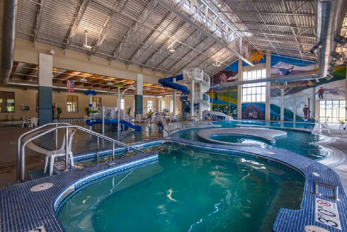 This vibrant interior image features children playing in a large swimming pool, with water slides and colorful murals in the background. The lively scene captures the playful atmosphere of a family-friendly recreation center, filled with energy and excitement.
