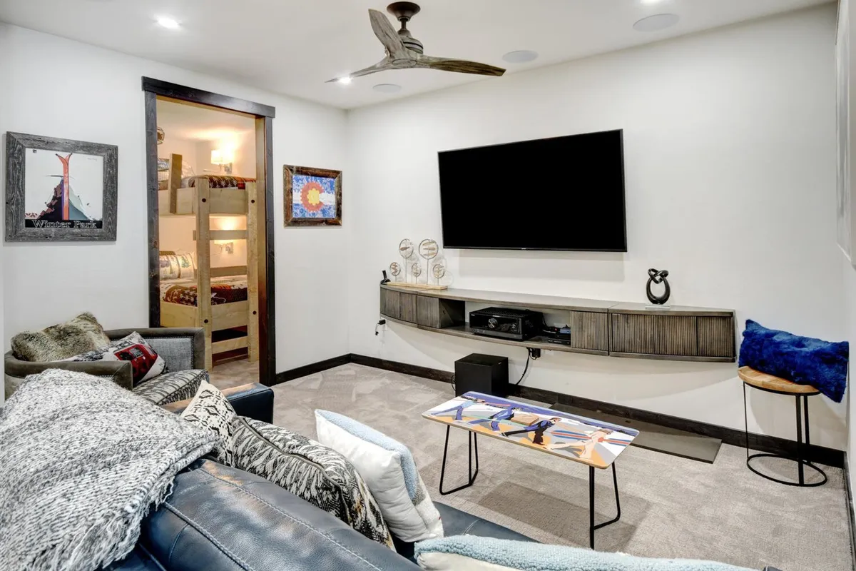 A comfortable family lounge with a mounted TV, a plush couch adorned with decorative pillows, vibrant artwork on the walls, and a patterned coffee table in the center. The space radiates a relaxed, playful atmosphere ideal for watching movies, playing games, or gathering with family and friends.